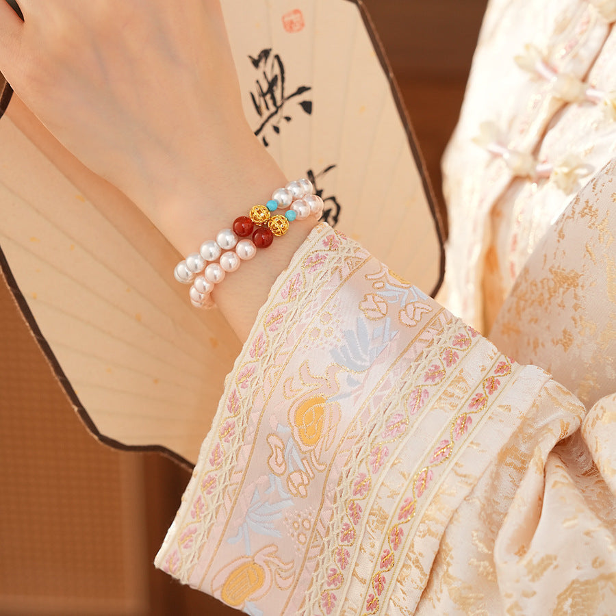 White/blush Shijia pearl bracelet featuring a red agate bead, gold zircon bead, and small blue accent — Trio Charm Pearl Bracelet by Glazenya.