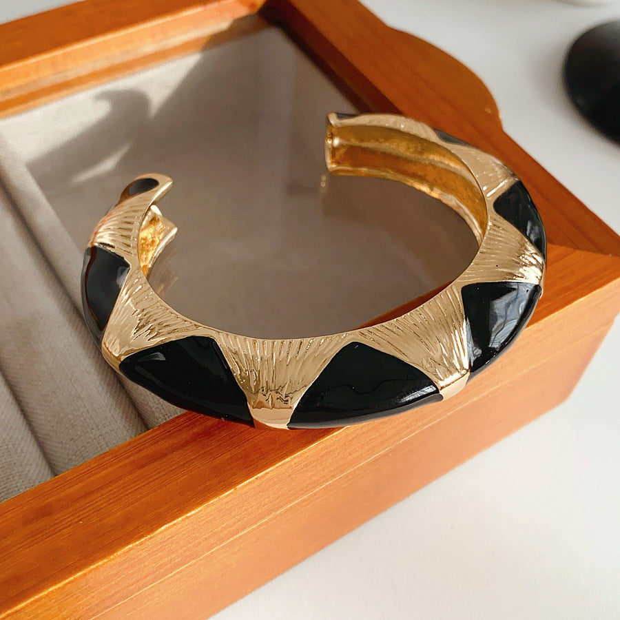 Gold-tone open cuff with triangular glossy enamel peaks; three variants (black, white, red) — Harlequin Enamel Cuff.